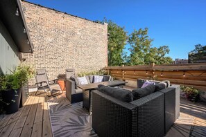 Une terrasse extérieure avec un mur en briques, une plateforme en bois et du mobilier d’extérieur comprenant un canapé et des fauteuils.