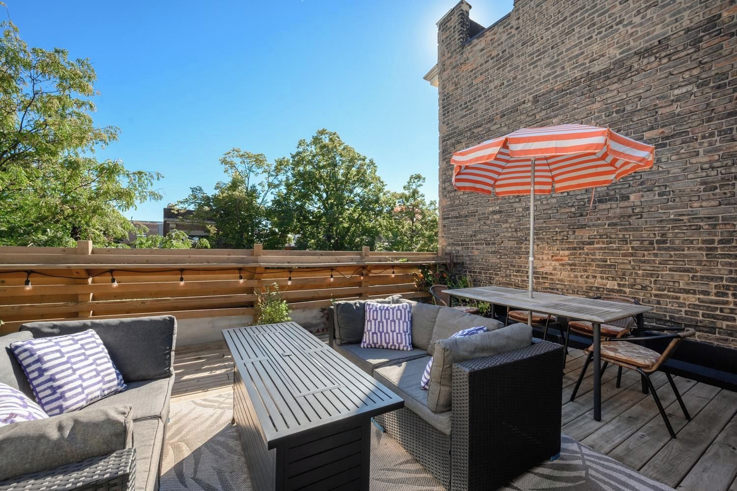 An outdoor patio with a brick wall, wooden deck, and outdoor furniture including a table and chairs.