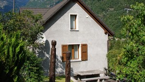 Une petite maison avec un toit en pente, une fenêtre avec des volets et un banc en pierre à l’extérieur.