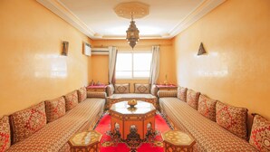 A traditional Moroccan room with a central seating area, a chandelier, and a large window with curtains. - A change of scenery guaranteed: TV apartment, WIFI, Car park (Marrakech)