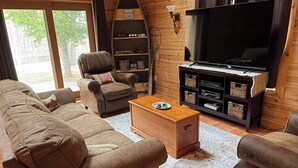 A living room with a sofa, armchair, coffee table, TV, and wooden shelves. - Nature lovers paradise w/direct access to lake,  trails & ample trailer parking. (Atlanta)