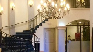 En imponerende trappe med sort gelænder, der fører op til en etage. En stor lysekrone hænger fra loftet, og væglamper giver lys.