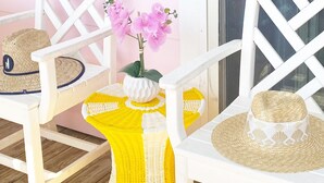 A white chair with a woven seat and backrest, a woven table with a yellow and white pattern, and a potted orchid on the table.