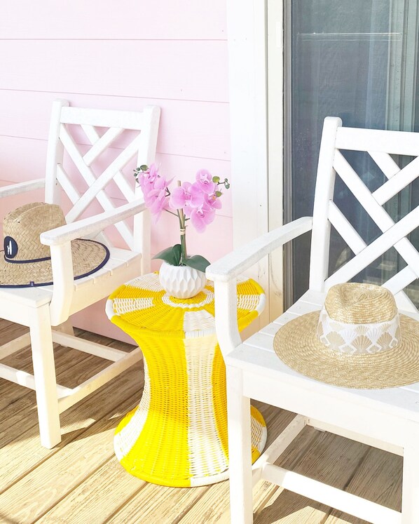 A white chair with a woven seat and backrest, a woven table with a yellow and white pattern, and a potted orchid on the table. - Little Pink Cottage OBX - Steps Away from Private Beach Access! (Nags Head)