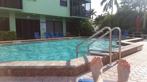 A swimming pool with a metal ladder, lounge chairs, and a building with a 'NO DIVING' sign in the background. - "WATERFRONT CONDO RENTAL" (Bonita Springs)