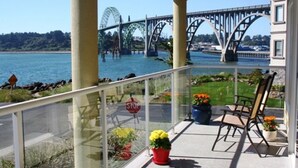 A balcony with a view of a bridge over water, potted plants, and outdoor seating.