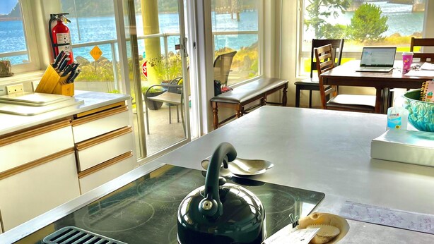 A kitchen with a kettle on the stove, a laptop on a table, and a view of a bridge and water outside.