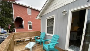 Une terrasse en bois avec une table et deux chaises, une maison rouge en arrière-plan et une maison grise dotée d’une porte-fenêtre coulissante.
