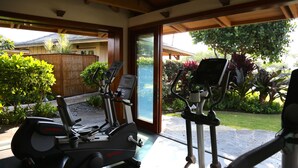 Un gimnasio en casa con bicicletas estáticas y una cinta de correr, ventanas amplias y vistas a un jardín.