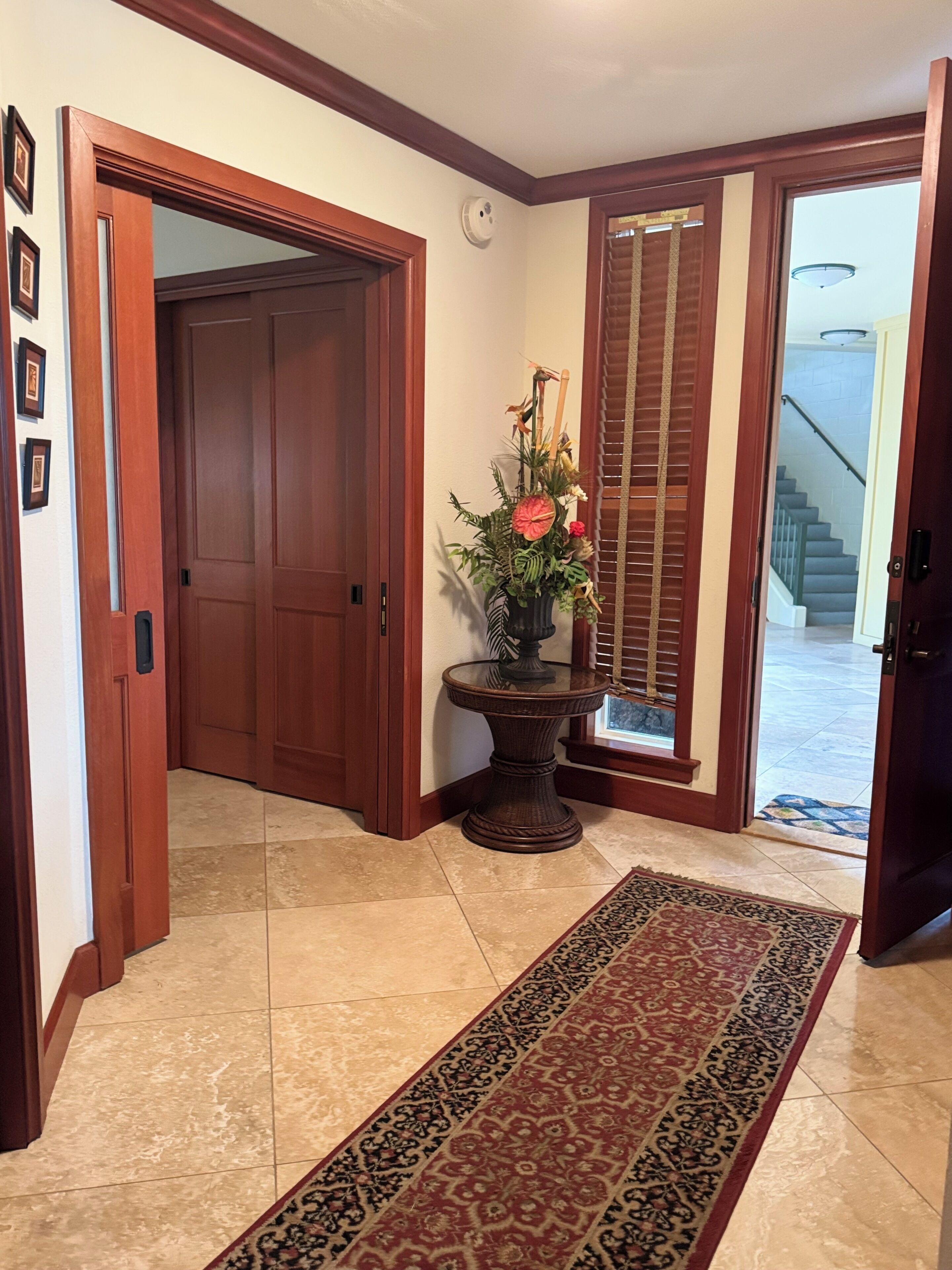 A hallway with a wooden door, a glass table with a floral arrangement, and a patterned rug.