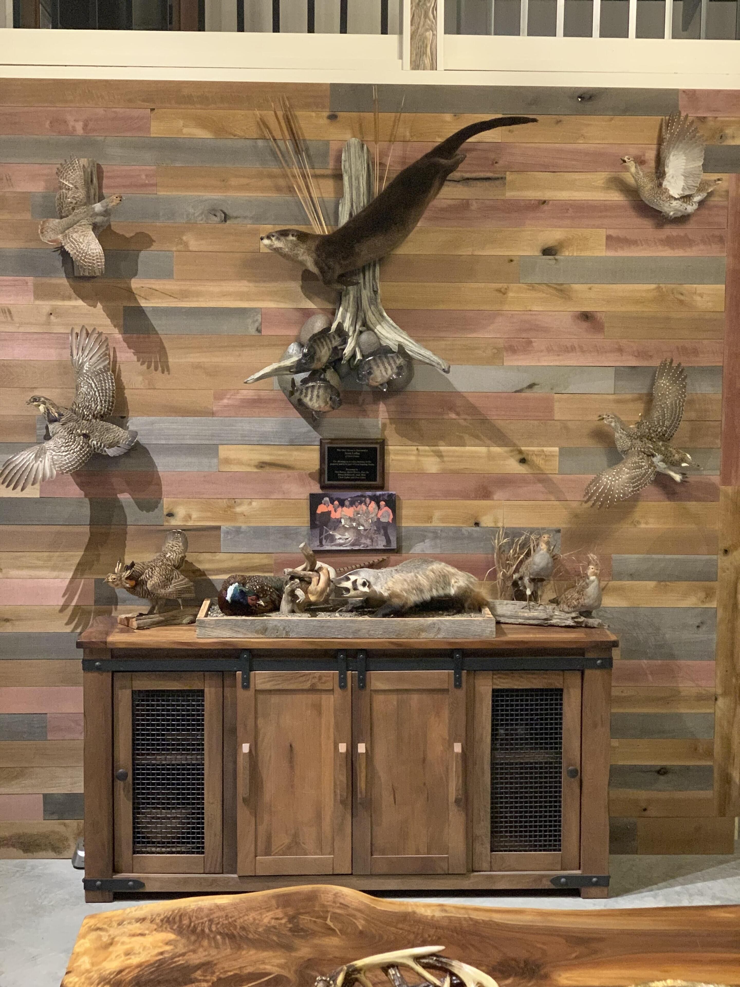 Een houten kast met daaraan bevestigde gevogelte- en dierentuigenstand, een ingelijste foto en een plaquette aan een muur.