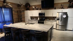 Une cuisine moderne dotée d’un grand îlot central, de tabourets de bar, d’appareils électroménagers en acier inoxydable et d’éléments décoratifs fixés au mur.