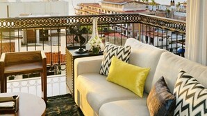 Ein Balkon mit einer weißen Couch, gelb gemusterten Kissen, einem kleinen Tisch und einer dekorativen Vase.