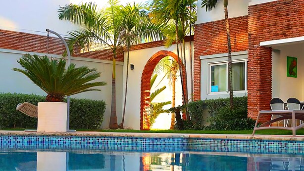 Un área de piscina moderna con piscina cristalina, un edificio de ladrillo y palmeras.