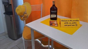 Una mesa con una botella de ron y una carta, una silla con un cojín amarillo, y un dispensador de agua.