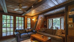 A cozy cabin interior with a wooden ceiling, a fireplace, a large window, and a leather sofa. - Charming Chalet-Private Cedar Soaking Tub-Snowline-Owner Managed (Glacier)
