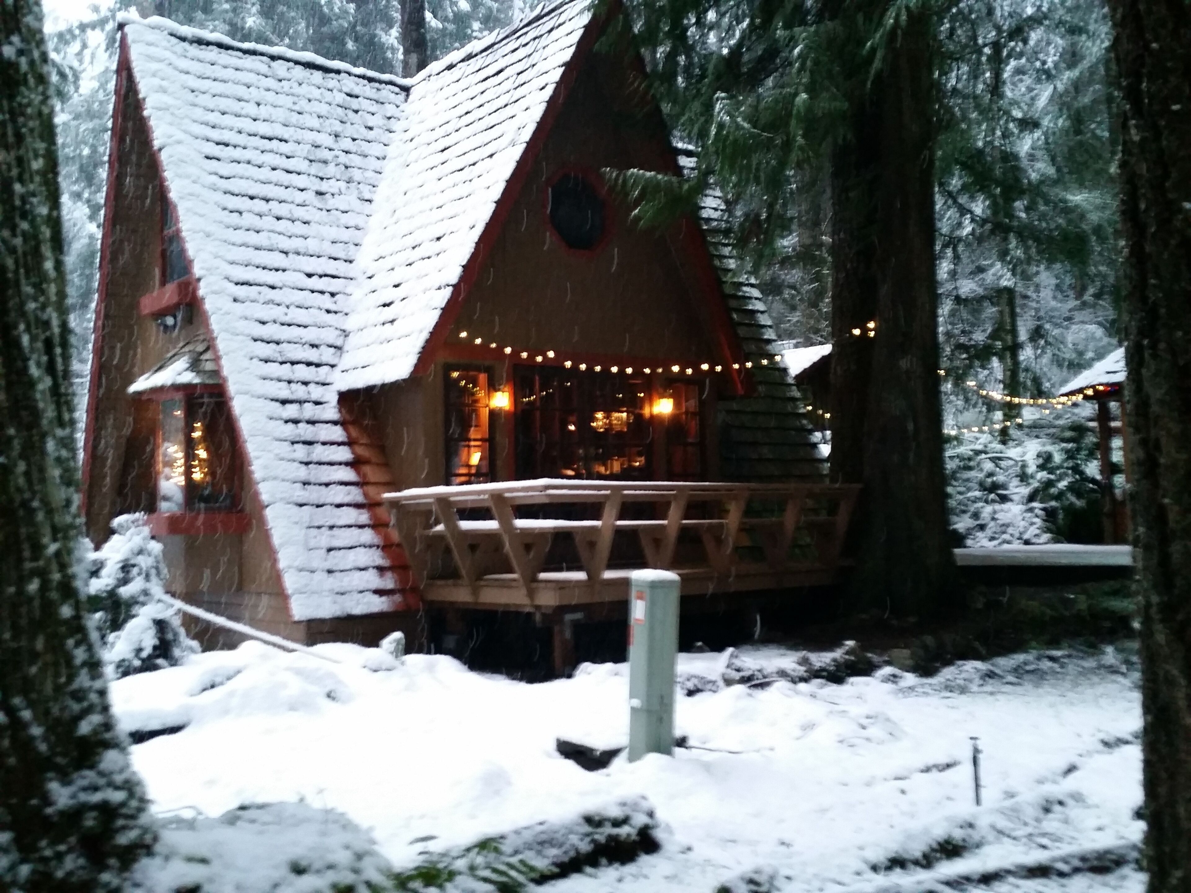 Eine Hütte mit schneebedecktem Dach und einer Terrasse mit Lichterketten.