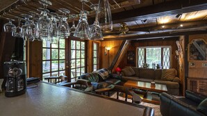 A cozy interior with a wooden ceiling, a bar area with a coffee maker, and a seating area with a sofa and chairs. - Charming Chalet-Private Cedar Soaking Tub-Snowline-Owner Managed (Glacier)