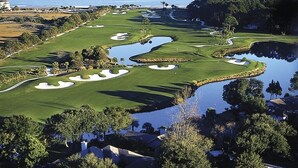 A golf course with sand bunkers, water hazards, and a view of the ocean.