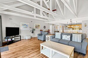 A spacious living room with a large grey sofa, a wooden coffee table, and a flat-screen TV.