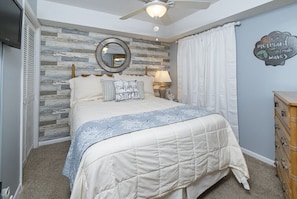 A bedroom with a bed, a ceiling fan, a mirror, a dresser, and a wall with a decorative sign. - Beautiful Ocean Front 3 Bedroom! (North Myrtle Beach)