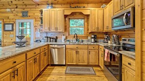 Una cocina estilo cabaña de madera, con armarios de madera, lavavajillas de acero inoxidable, microondas y un ventanal grande.