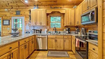 Una cocina estilo cabaña de madera, con armarios de madera, lavavajillas de acero inoxidable, microondas y un ventanal grande.