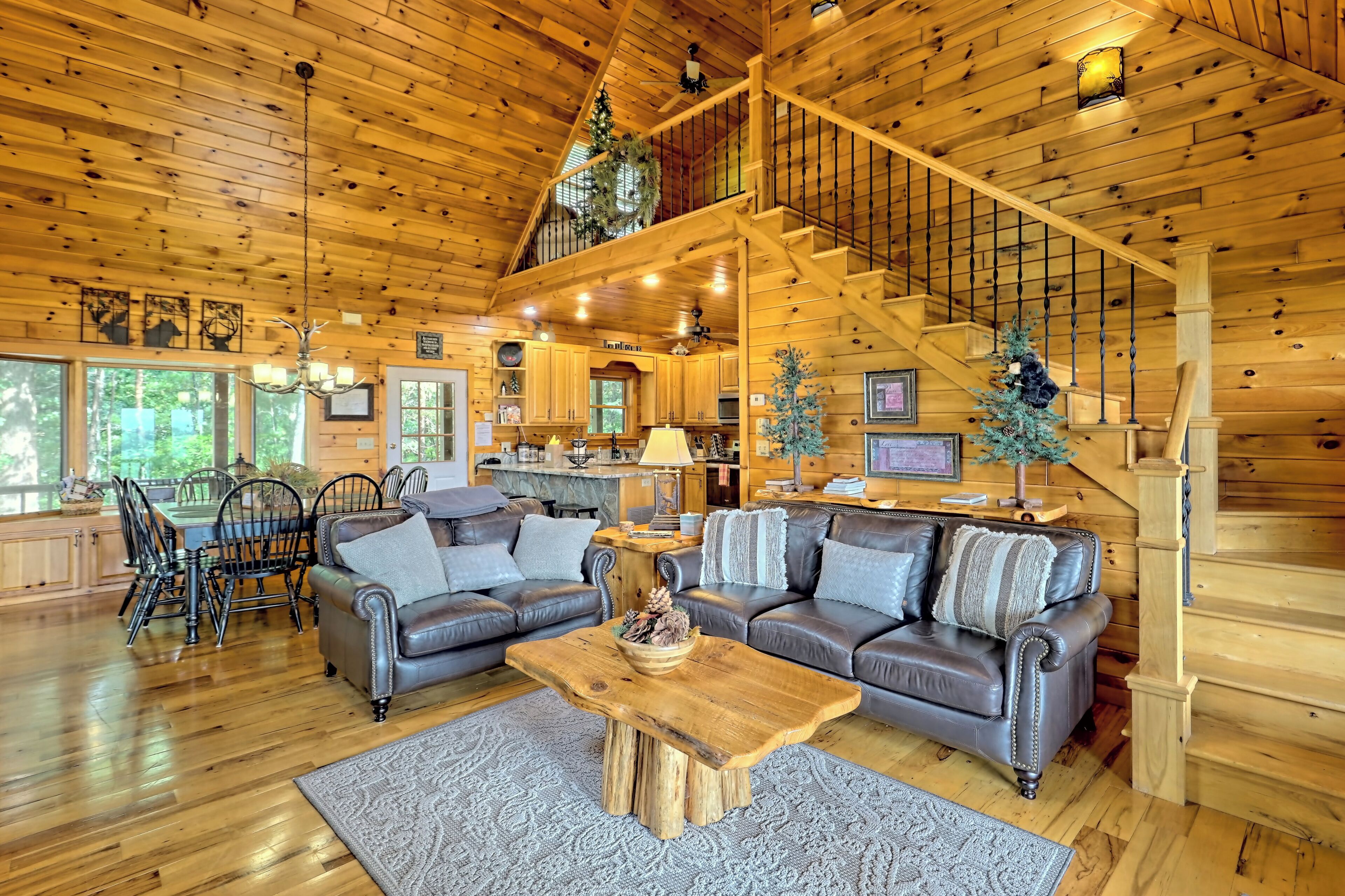A spacious living room with a wooden ceiling, a dining area with a table and chairs, and a staircase leading to an upper level.