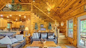 Un interior de cabaña espacioso con una escalera de madera, una sala de estar acogedora con un sofá de cuero, una mesa de comedor y una cocina con armarios de madera y un microondas.