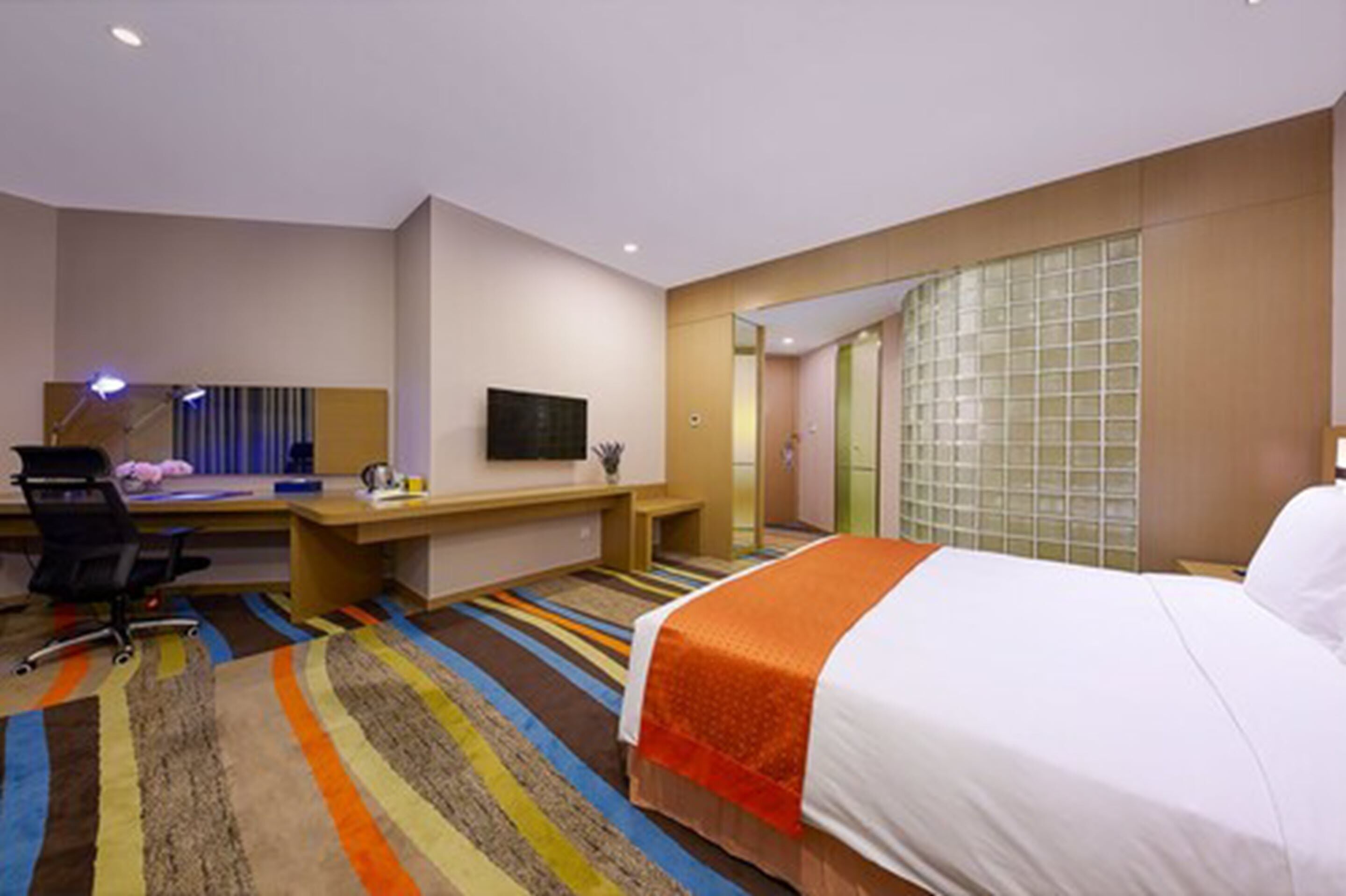 Habitación de hotel con cama, escritorio, silla, televisor y alfombra a rayas.