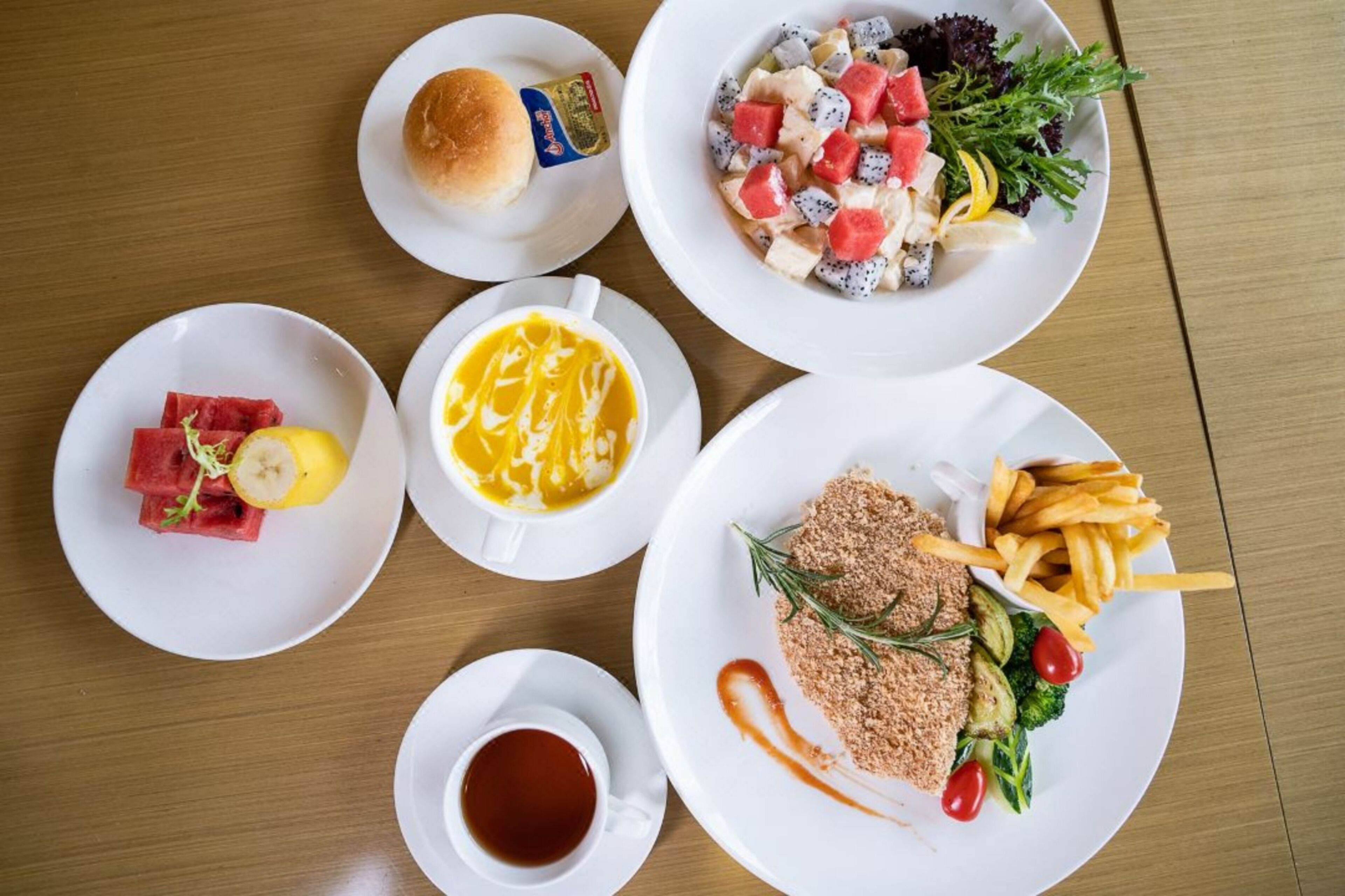 Ein Tisch mit verschiedenen Speisen, darunter ein Salat, ein Sandwich, ein Dessert und ein Teller mit Pommes und Gemüse.