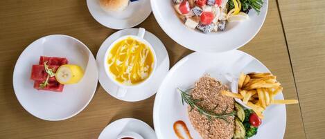 Une table avec différents plats, notamment une salade, un sandwich, un dessert et une assiette de frites et de légumes.