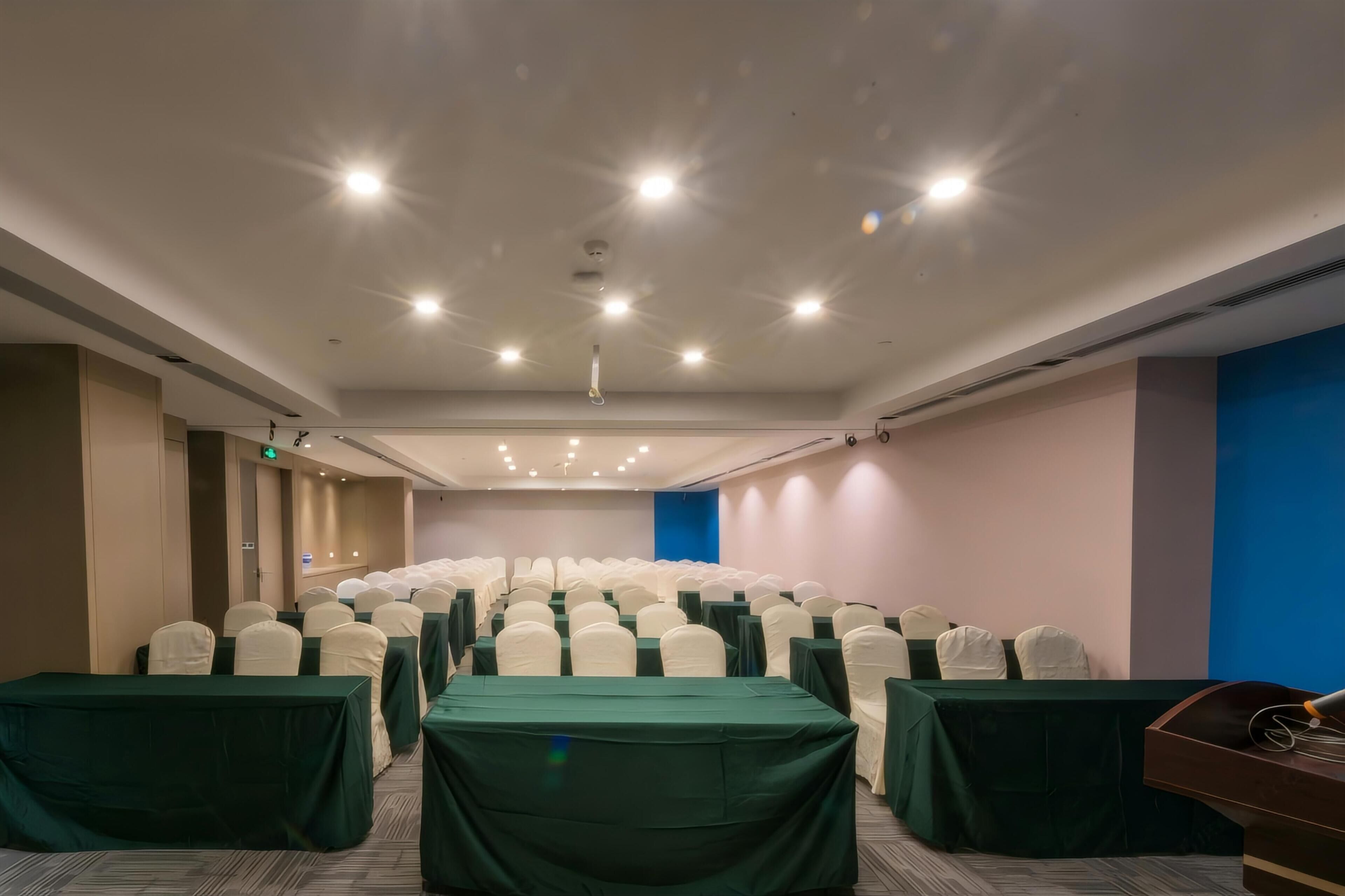 Une salle de conférence avec des rangées de chaises, des tables et un pupitre.