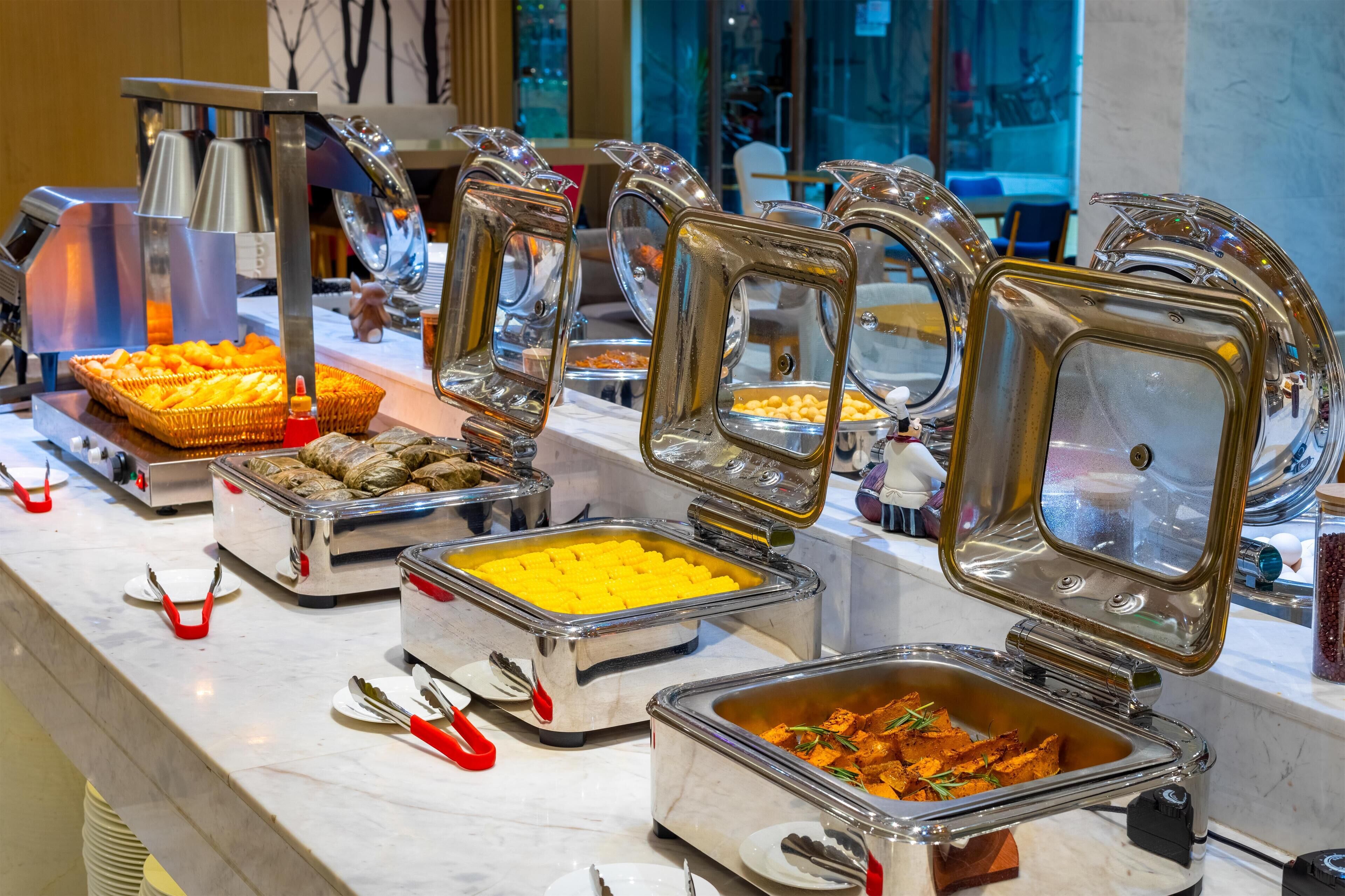 Een buffet met diverse gerechten, waaronder sinaasappelpartjes, gele custard en sinaasappelkip, gepresenteerd op een marmeren toonbank.