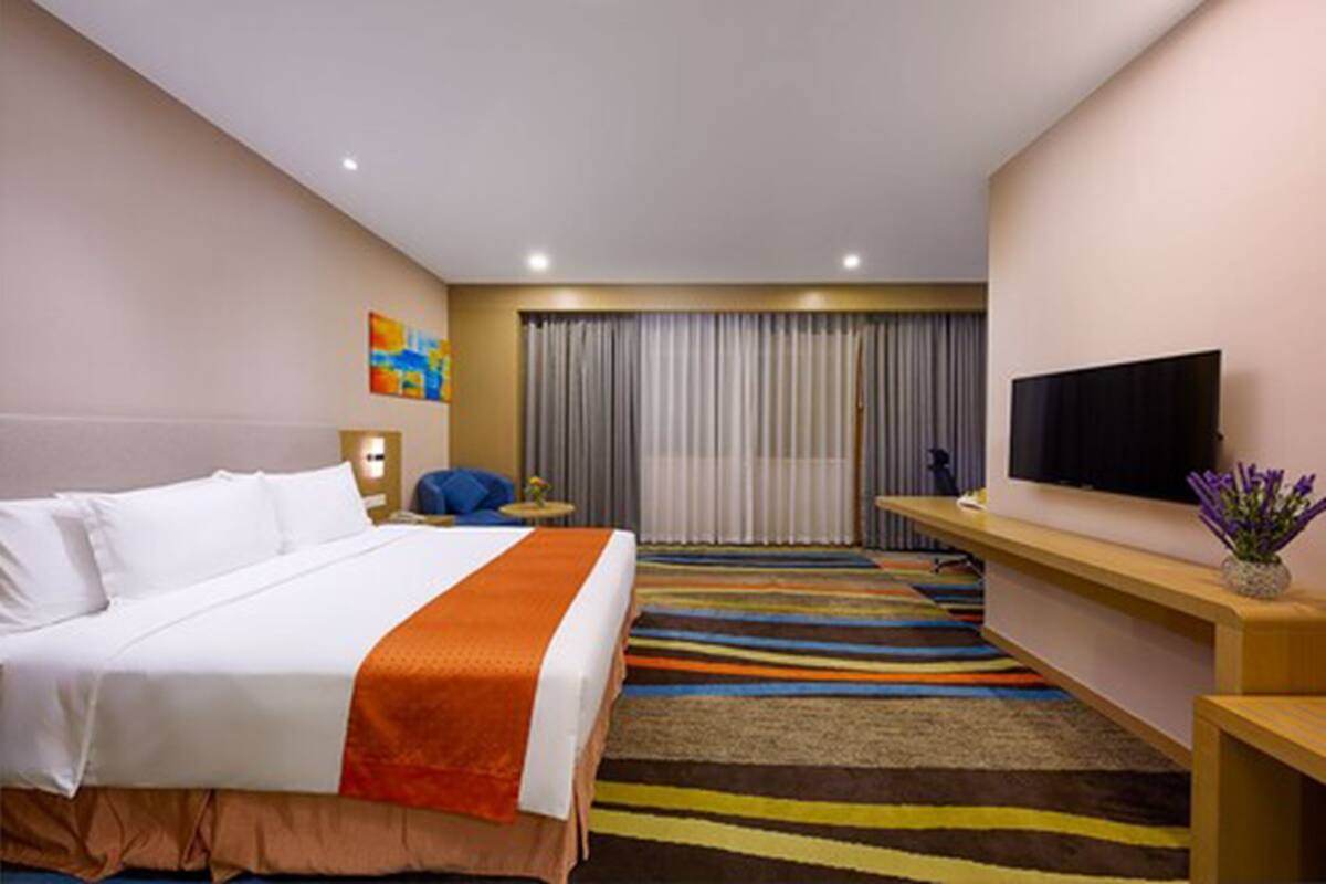 Une chambre d’hôtel avec un lit, une télévision, un bureau et une moquette rayée aux couleurs vives.