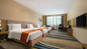Ein Hotelzimmer mit zwei Betten, einem Schreibtisch, einem Stuhl, einem Fernseher und einem großen Fenster mit Vorhängen.