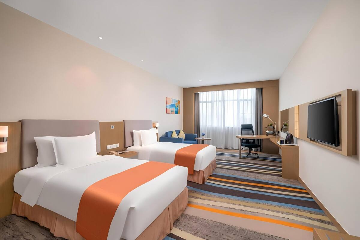 Une chambre d’hôtel avec deux lits, un bureau, une télévision et une grande fenêtre.