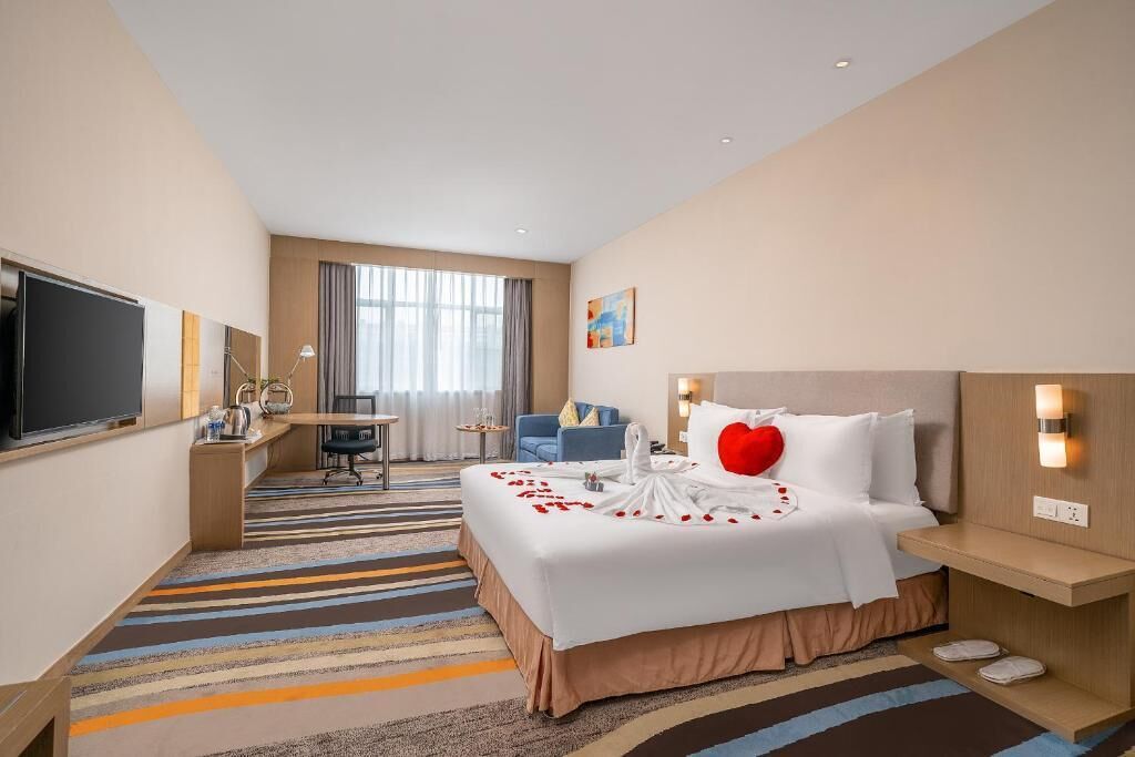 Ein Hotelzimmer mit einem großen Bett, einem Schreibtisch, einem Fernseher und einem Fenster mit Vorhängen.
