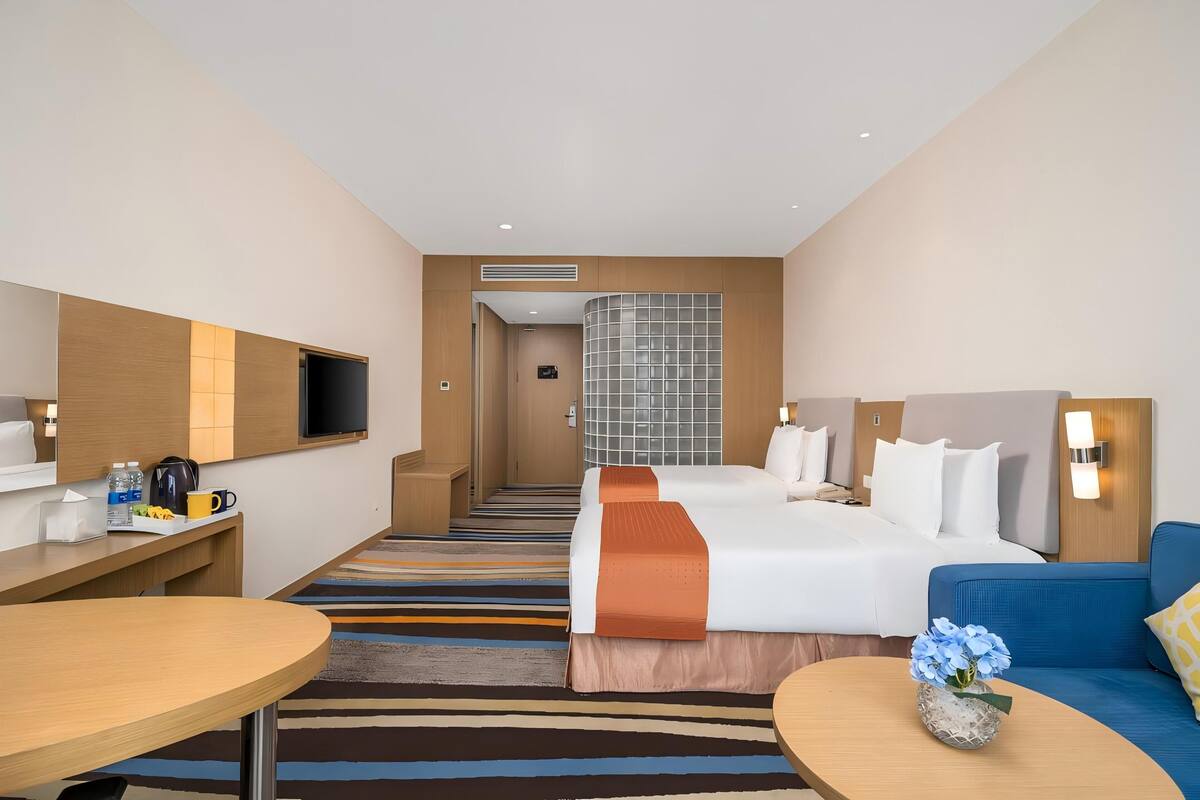 Une chambre d’hôtel avec un lit, un bureau, une télévision, un canapé et une petite table sur laquelle est posé un vase de fleurs.