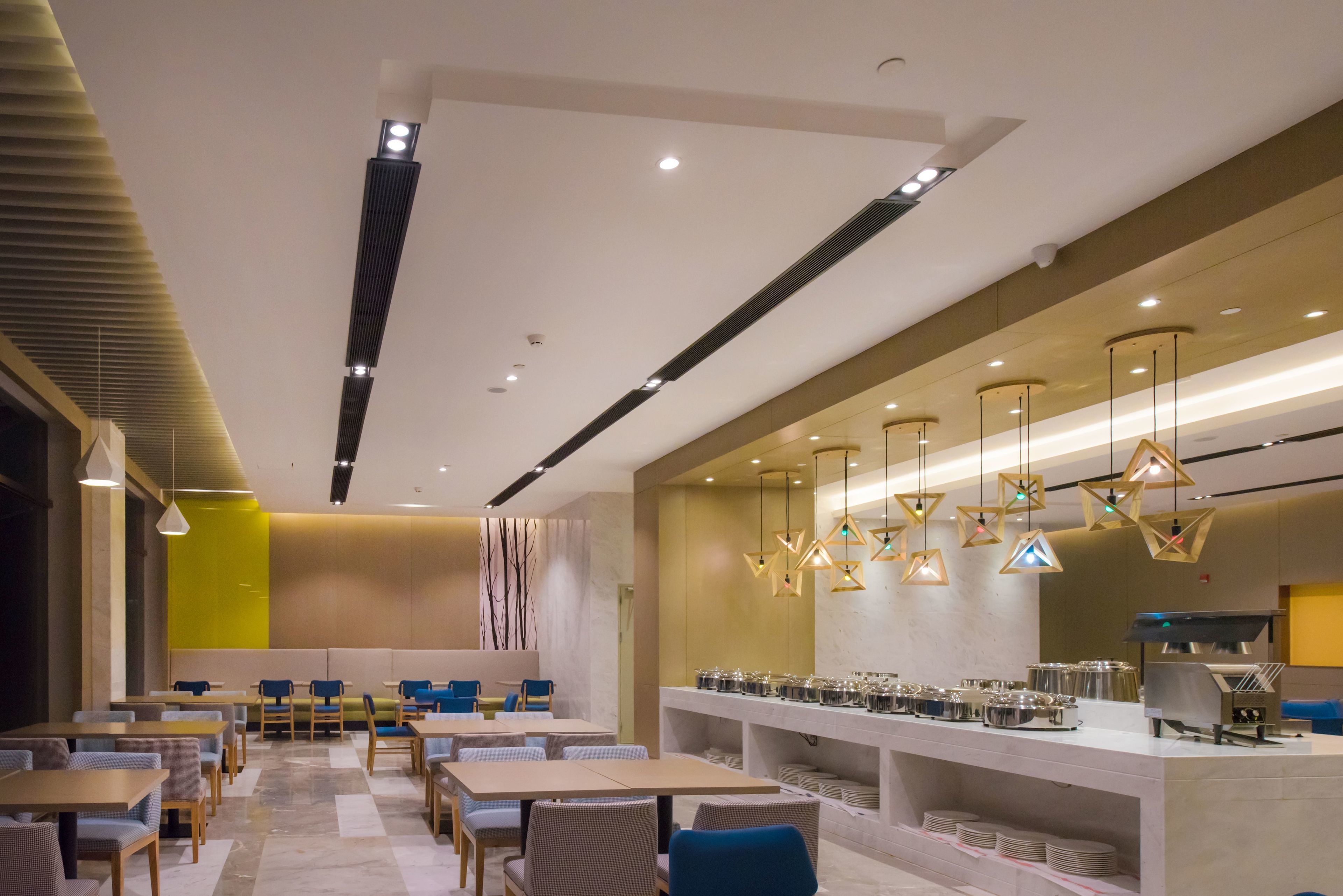 A modern restaurant with a long counter, multiple seating areas, and a variety of lighting fixtures.