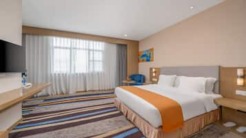 A hotel room with a large bed, a desk, a TV, and a window with curtains.