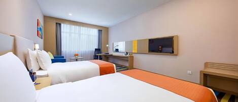 Une chambre d’hôtel avec deux lits, un bureau, une chaise, une petite table avec des fleurs, une télévision et une fenêtre avec des rideaux.