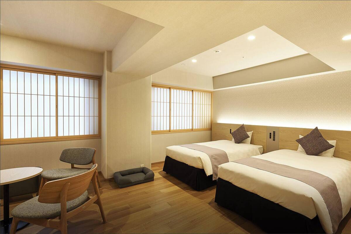 Habitación de hotel con dos camas, una mesita, una silla y un sofá cama.