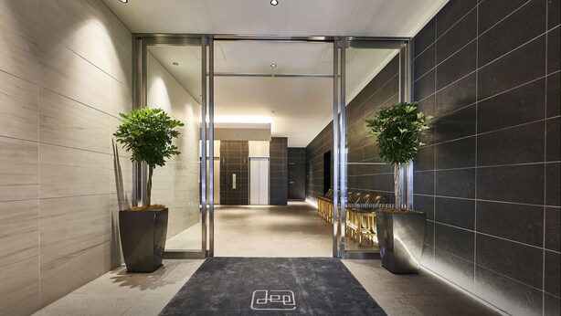 A modern hotel lobby with a glass door entrance, a reception desk, and potted plants. - DEL style Osaka - Shinsaibashi by Daiwa Roynet Hotel (Osaka)