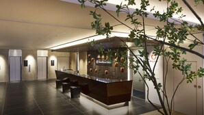 A modern hotel reception area with a reception desk, elevators, and a large potted plant. - DEL style Osaka - Shinsaibashi by Daiwa Roynet Hotel (Osaka)