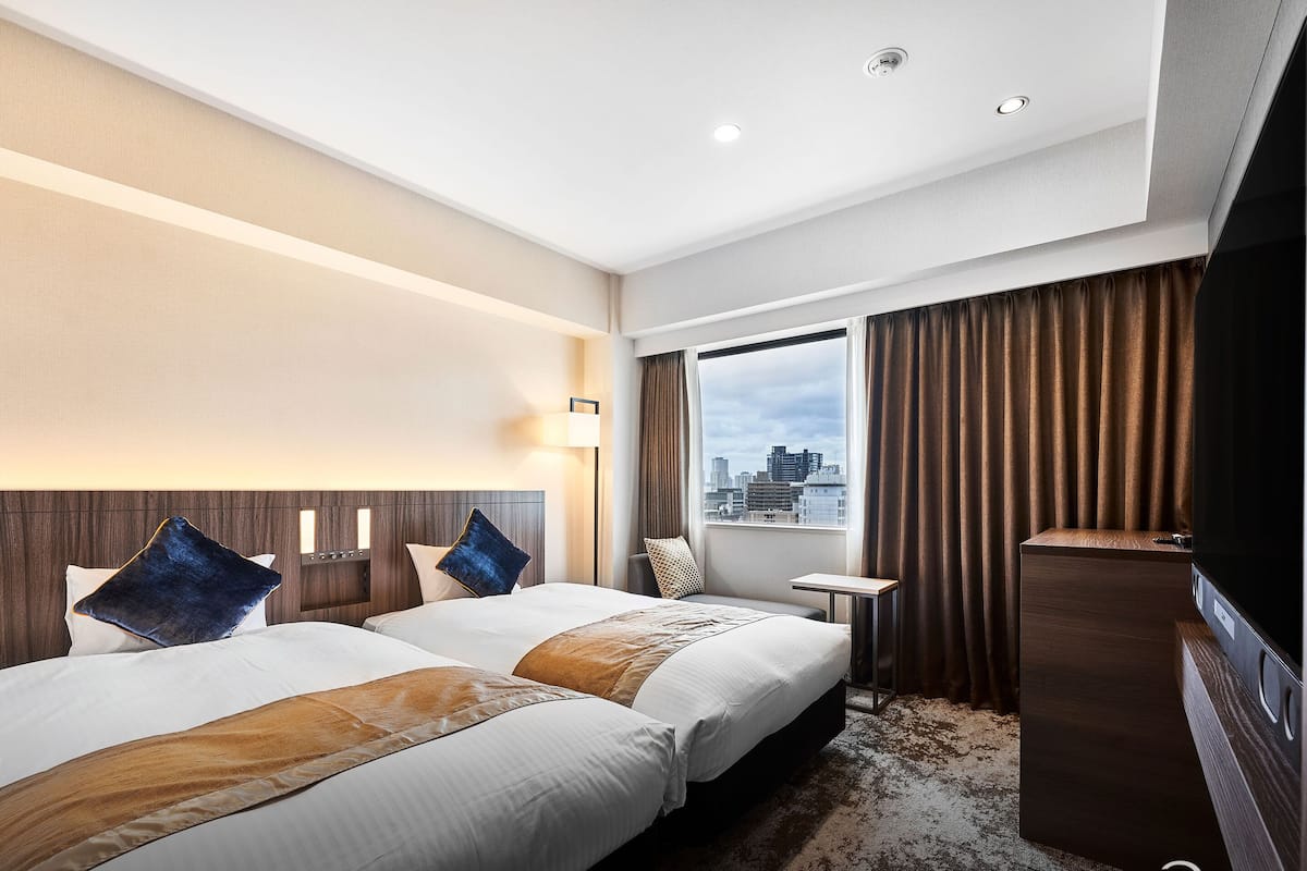 Habitación de hotel con dos camas, vistas a la ciudad, un escritorio y un televisor.
