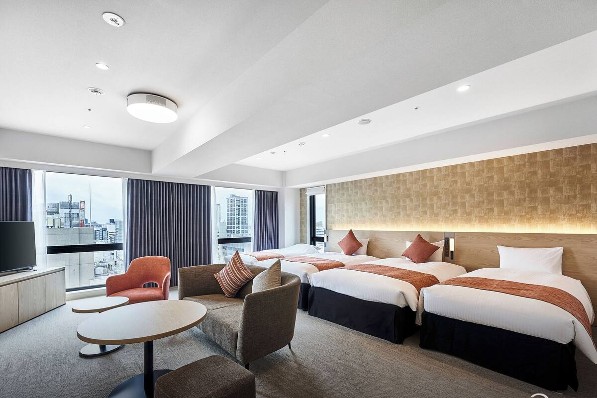 Habitación de hotel moderna con vista a la ciudad, dos camas, un escritorio y un área de descanso.