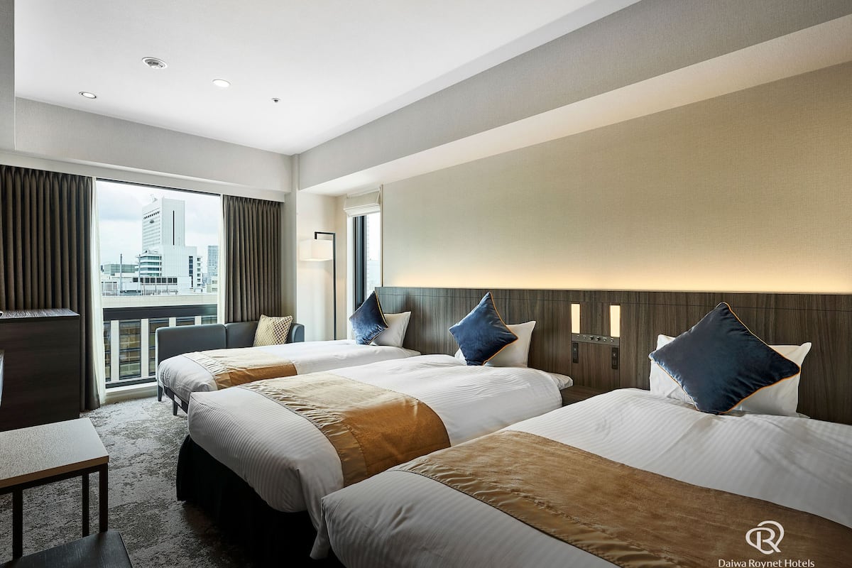 Habitación de hotel con tres camas, un escritorio y vistas a la ciudad.