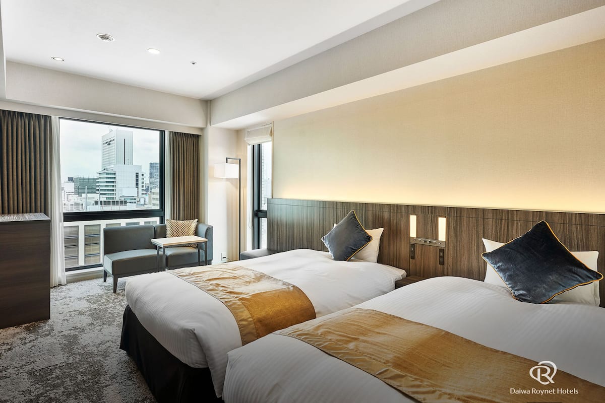 Habitación de hotel con dos camas, un escritorio, una silla y vistas a la ciudad.