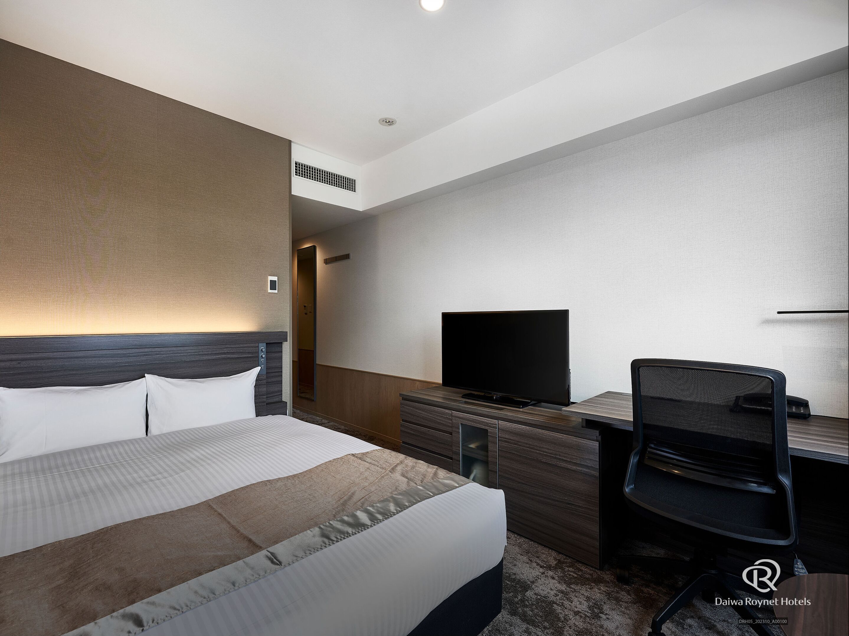 A hotel room with a bed, a desk, a chair, a television, and a mirror.